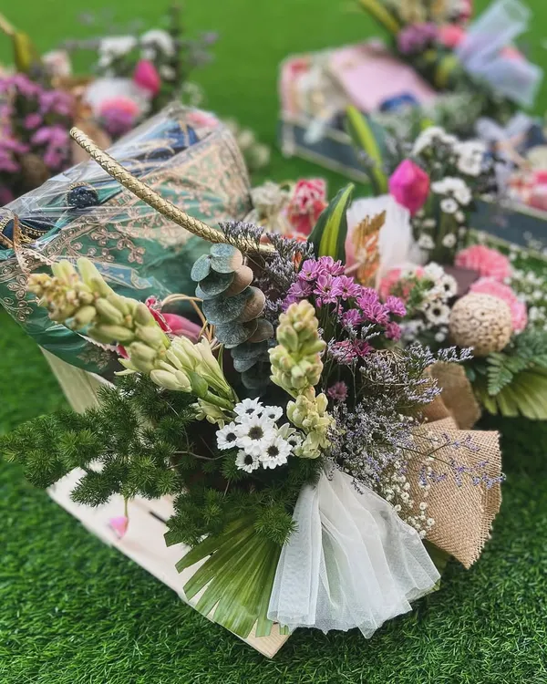 This luxurious hamper combines traditional elegance with natural textures. A printed saree is styled in a jute basket with an abundance of fresh, wild-looking florals, creating a gift that feels both opulent and organic.