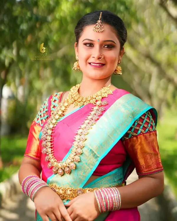 A bright, joyful outdoor portrait showcasing a stunning pink and turquoise silk saree. We use natural light to bring out the rich colors of the fabric and the genuine smile of our client, creating a classic and happy memory.