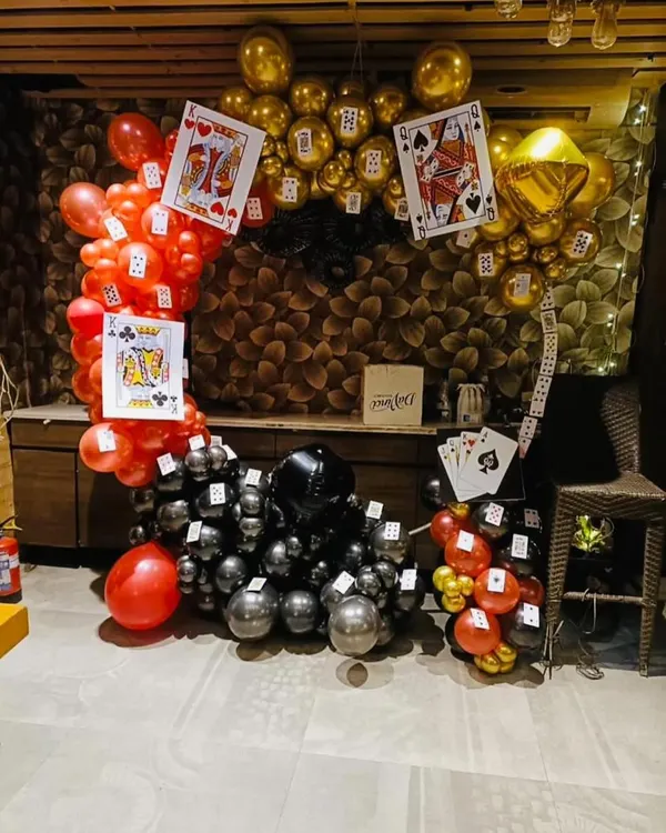 A casino-themed card party decoration, perfect for Diwali or a milestone birthday. This setup features a balloon arch in red, black, and gold, decorated with large playing cards.
