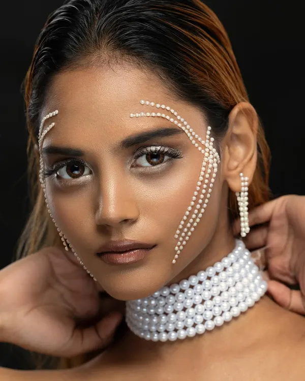 An editorial beauty portrait with a model adorned with pearls on her face and a pearl choker, showcasing a creative and high-fashion makeup look.