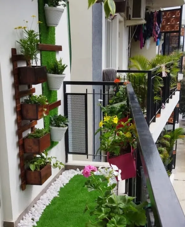 A complete balcony transformation featuring a custom-built vertical planter, artificial grass with a white pebble border, and colorful railing planters to maximize greenery.