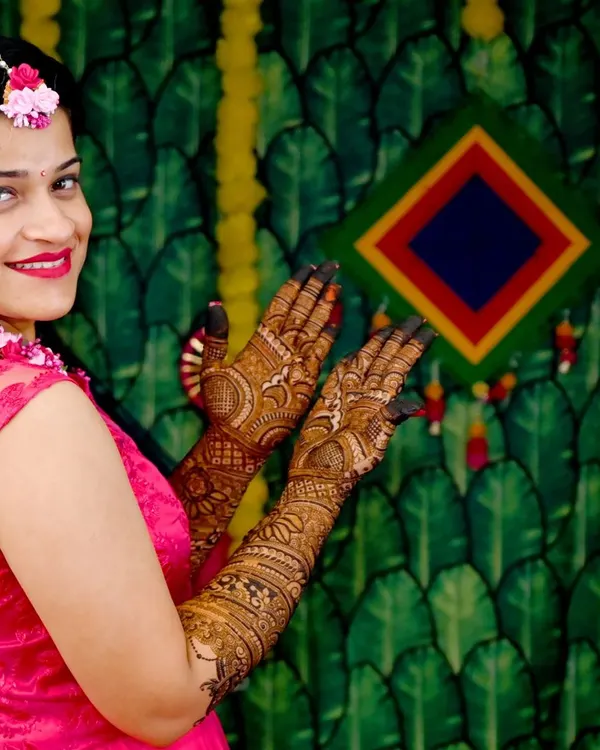 A beautiful bride showing off her full-sleeve mehendi. The rich, dark paste promises a fantastic stain, and her smile says it all.