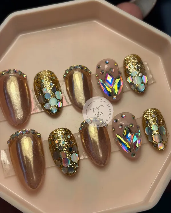 A set of glamorous, party-ready press-on nails. This custom design features gold chrome, chunky glitter, and nails fully encrusted with large, iridescent geometric crystals.