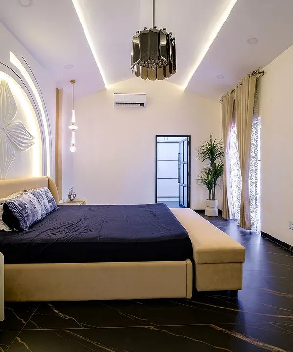 This master bedroom is a study in modern luxury. The dramatic arched headboard features a 3D floral relief, beautifully illuminated to create a soft glow. The dark marble flooring provides a stunning contrast to the light, neutral tones of the bed and walls.