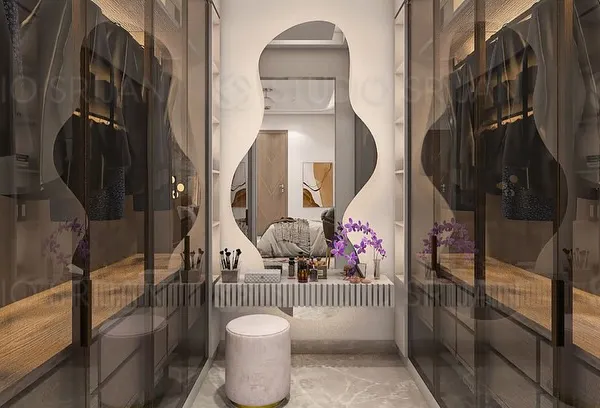 A dedicated dressing and vanity area, featuring a beautifully lit, organically shaped mirror. The walk-in closet is visible through smoked glass doors, creating a sense of depth and luxury.