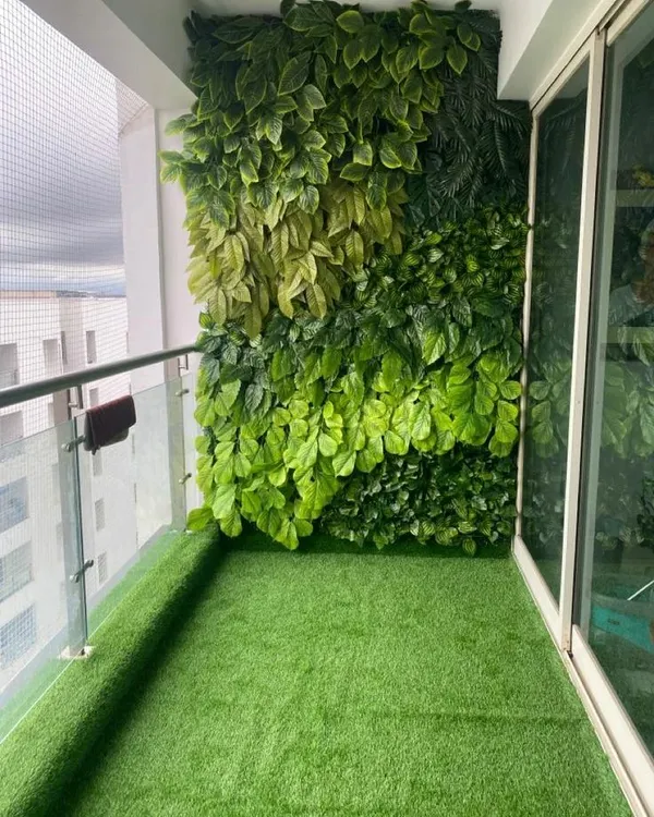 A complete balcony makeover featuring a dense artificial green wall for privacy and a soft artificial lawn, turning a standard balcony into a private garden.