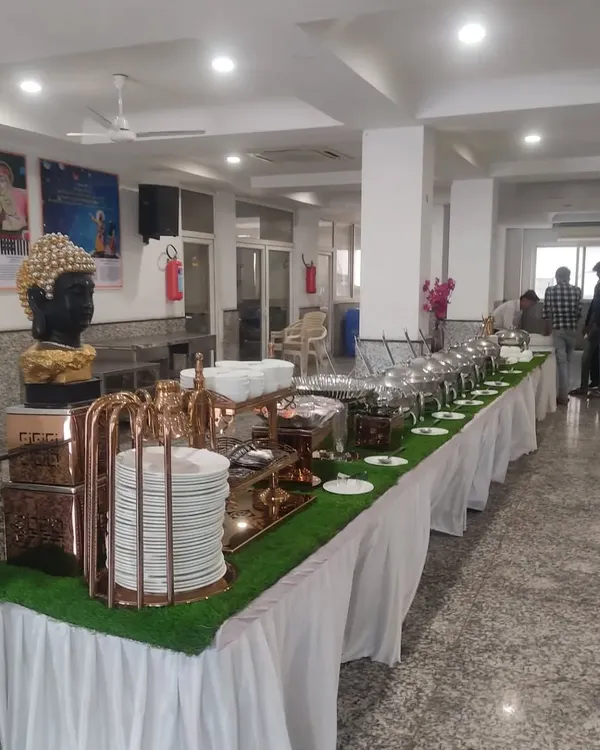 A clean and professional buffet setup for a corporate lunch. We use a long table with crisp white skirting, an artificial grass runner for a touch of green, and elegant chafing dishes to keep the food warm.