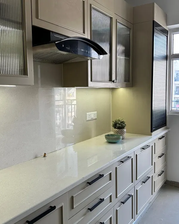 A sleek and modern kitchen at our Nirala Estate project, featuring beige paneled cabinets, black hardware, and fluted glass upper cabinets for a touch of texture.
