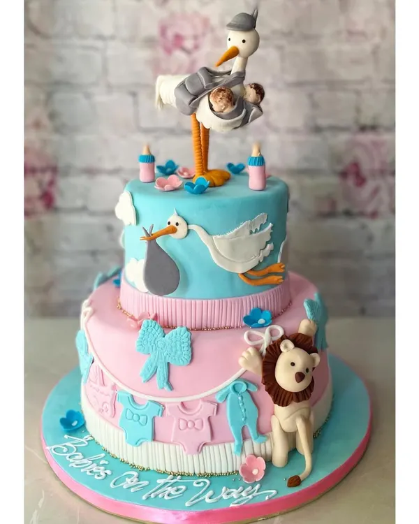 A spectacular two-tier cake for a twin baby shower! The design features a stork delivering two babies, with adorable pink and blue details. We love creating these elaborate, story-telling cakes.