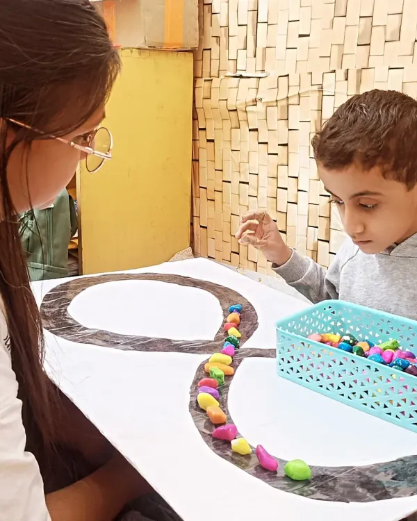 In our ABA therapy sessions, we use tactile activities to improve focus and fine motor skills. Here, a child carefully places colorful stones along a line, an exercise that builds concentration and hand eye coordination.