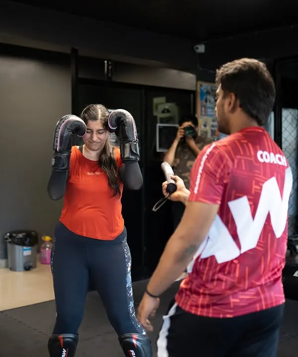 A coach provides instruction to a student during a boxing drill. This constant feedback is crucial for correcting mistakes and building proper technique.