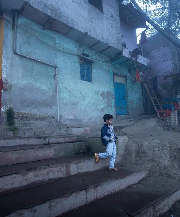 A young boy descends stone steps on a foggy morning at the Yamuna ghat, the mist creating a soft, painterly quality in this environmental shot.