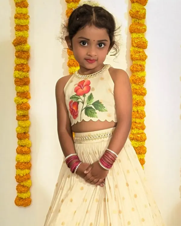 Presenting a handcrafted heirloom for your little one. This cream lehenga set features a halter-neck crop top with a unique, hand-painted red hibiscus motif, paired with a flowing skirt finished with a traditional Banarasi border. It's the perfect blend of modern design and timeless elegance for any celebration.