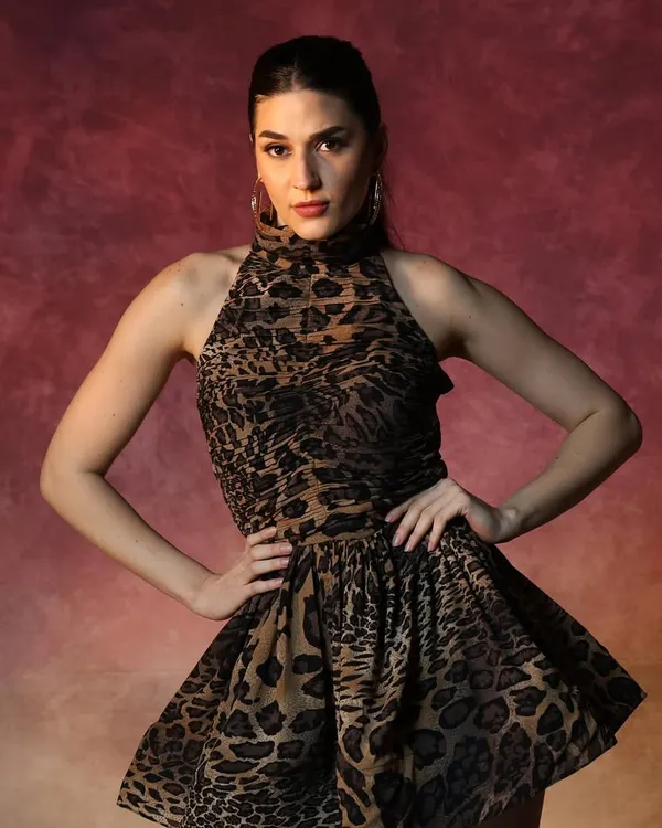A powerful shot from a fashion campaign. The makeup features a strong, defined brow and contoured cheekbones to create a striking look that complements the bold, animal-print dress and dramatic lighting.