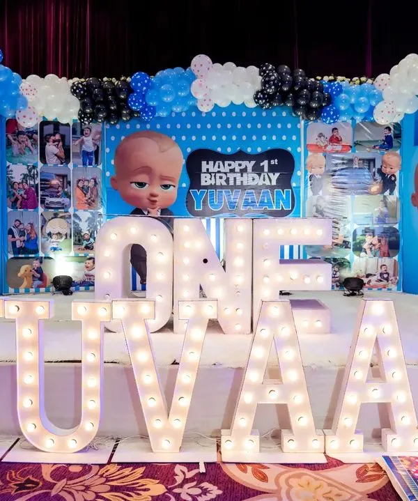 This Boss Baby first birthday stage was a huge hit. I used large marquee letters to spell out the name "YUVAAN" and created a custom backdrop filled with photos from his first year, surrounded by a blue, black, and white balloon garland.