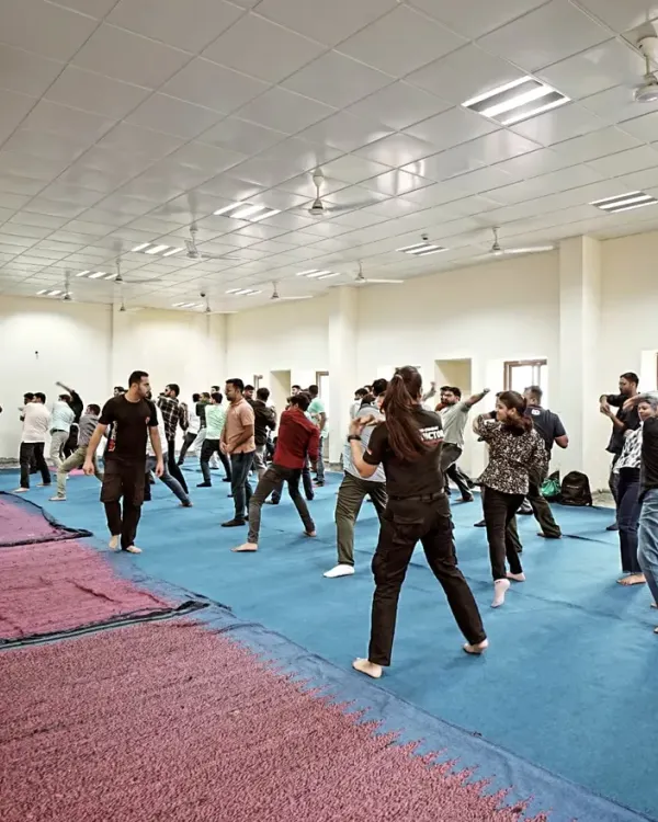 A mixed group of men and women practicing defensive stances in a large indoor session.