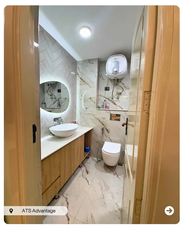 A clean and modern bathroom design featuring marble-finish tiles on the floor and walls. The floating wooden vanity, vessel sink, and backlit mirror create a spa-like feel.