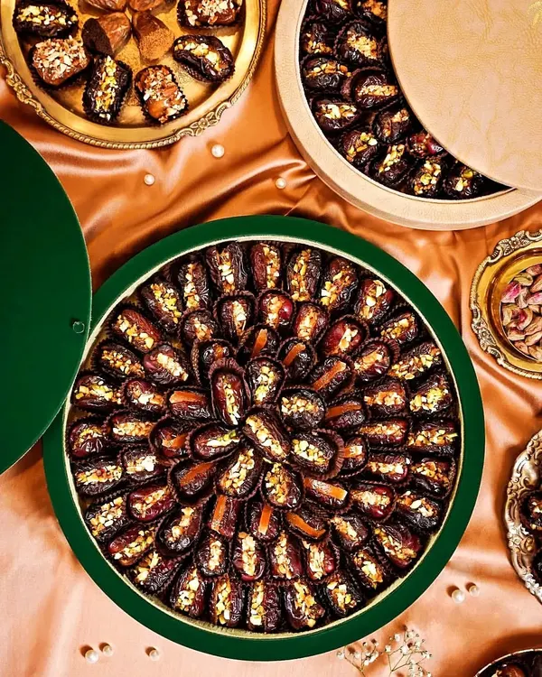 A luxurious flatlay of gourmet stuffed dates, arranged in beautiful circular patterns. The rich colors of the dates against the satin green fabric create an opulent and elegant visual.