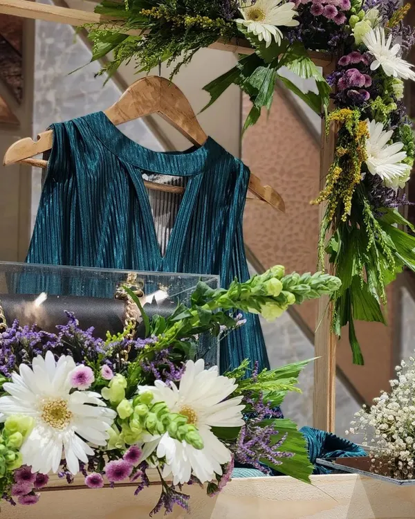 A close-up of one of our trousseau packing designs. We used a wooden frame to hang this teal pleated top, with a clear acrylic box to protect a luxury handbag below, all adorned with fresh white gerberas and purple statice.
