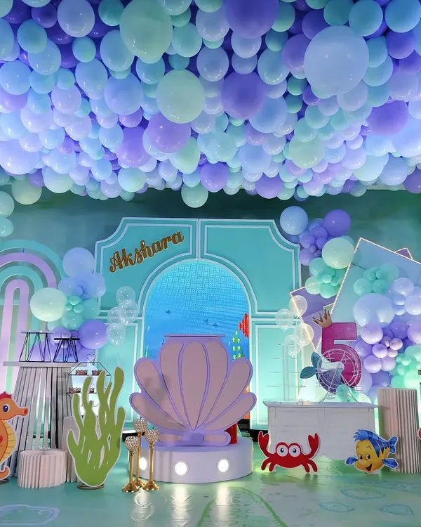 An immersive under-the-sea theme with a ceiling covered in blue and purple balloons to simulate water. The stage features a large shell prop and various sea creature cutouts.
