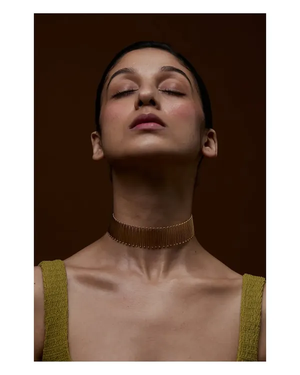 A serene and graceful portrait designed to highlight a statement choker. The model's closed eyes and the warm, earthy tones create a meditative mood, allowing the intricate gold jewellery to be the sole focus.