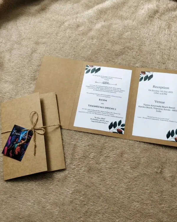 This tri-fold invitation is crafted from sturdy kraft paper, giving it a simple, rustic feel. It's tied with natural twine and features a small, colorful tag with a custom illustration of the couple.