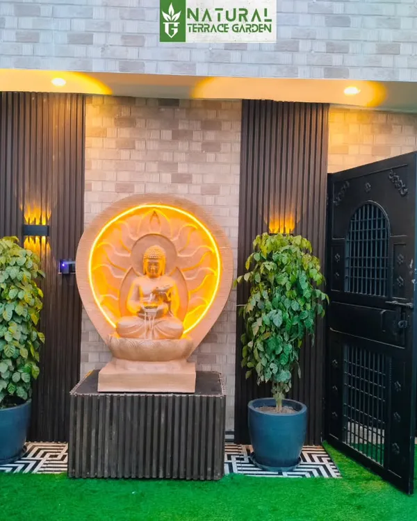 A serene entrance to a terrace garden in Uttam Nagar, featuring a custom-lit sandstone Buddha statue flanked by lush plants.