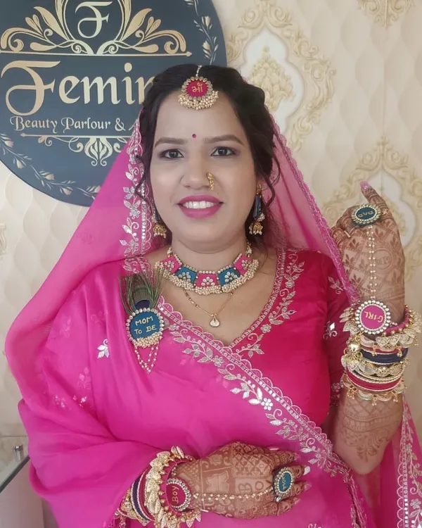 A beautiful look for a `Godh Bharai` or baby shower. The client is glowing in a traditional pink Marwari outfit, with "Mom to be" accessories and fresh, happy makeup.