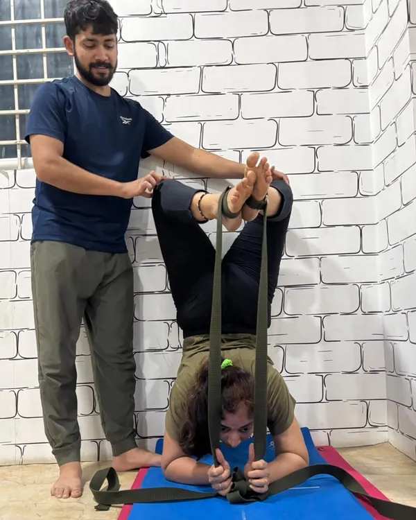 Using straps to achieve correct form in Pincha Mayurasana (Feathered Peacock Pose). I am providing support to ensure the student's shoulders and core are engaged correctly, building strength for the full inversion.