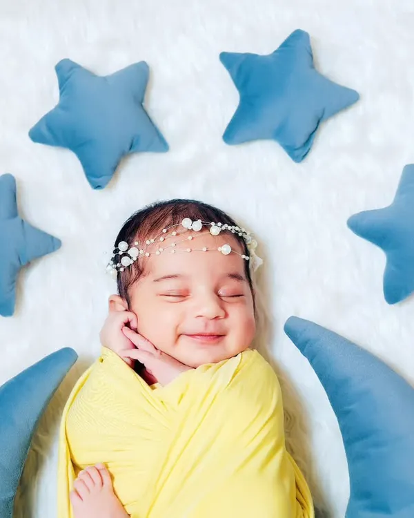 A happy, sleeping newborn swaddled in yellow, nestled on a crescent moon prop. We love capturing these little smiles during our newborn sessions.
