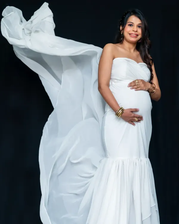 Pure elegance in the studio. This mom-to-be looks stunning in a white strapless gown, with the flowing fabric creating a sense of drama and grace against a simple black background.