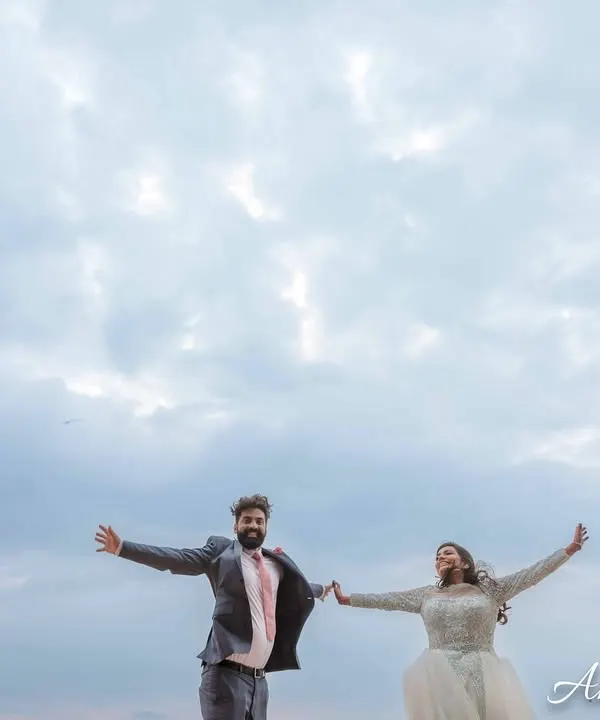 A joyful, carefree moment of a couple with their arms outstretched against a vast, cloudy sky. This shot captures a feeling of freedom and happiness.