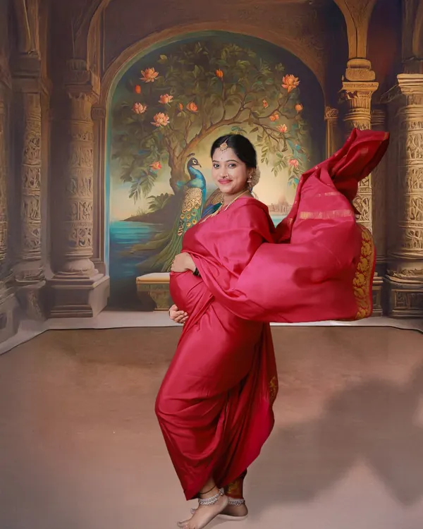 A vibrant and dynamic traditional maternity shoot. The mom-to-be is dressed in a beautiful red saree, with the fabric flowing to create a sense of movement against a painted palace backdrop.
