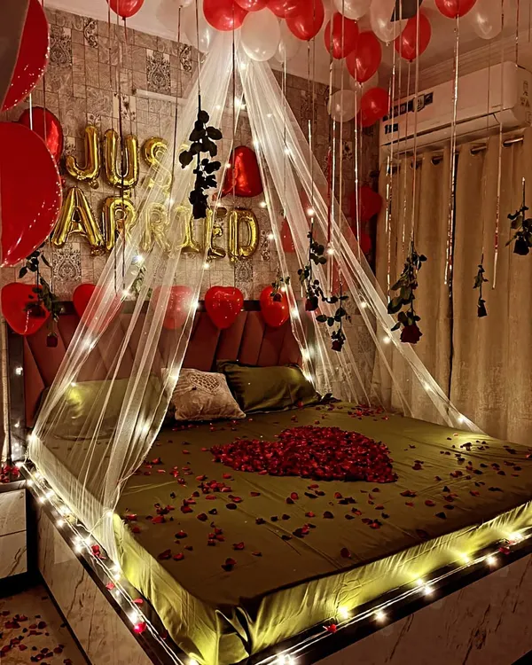 A closer look at the 'Just Married' bed canopy setup. You can see the detail of the fairy lights woven into the sheer fabric and the hanging black roses, which add a unique touch to the classic red and white theme.