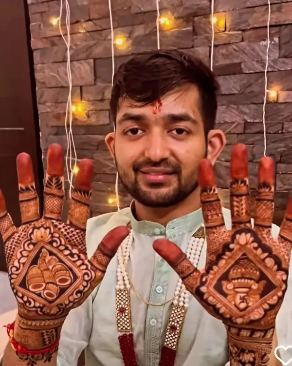 A handsome groom proudly displaying his mehendi, which features traditional symbols like the kalash and Lord Ganesha to bring blessings to his wedding.