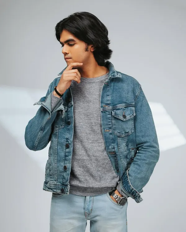 A classic men's fashion shot, featuring a denim jacket layered over a sweater. The thoughtful pose and clean lighting make this perfect for a brand's lookbook or catalog.