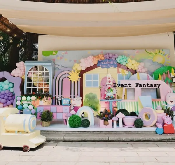 A full stage setup for Taashvi's Peppa Pig party. This vibrant and playful world includes Peppa's house, a colorful train, and cutouts of Peppa and her family, all in a cheerful pastel palette.