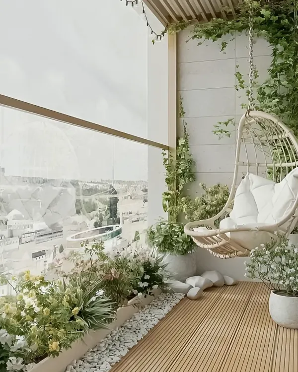 A serene and elegant balcony featuring a white wicker swing chair and lush climbing ivy. The wooden deck flooring and planter boxes filled with white flowers create a peaceful, garden-like atmosphere.