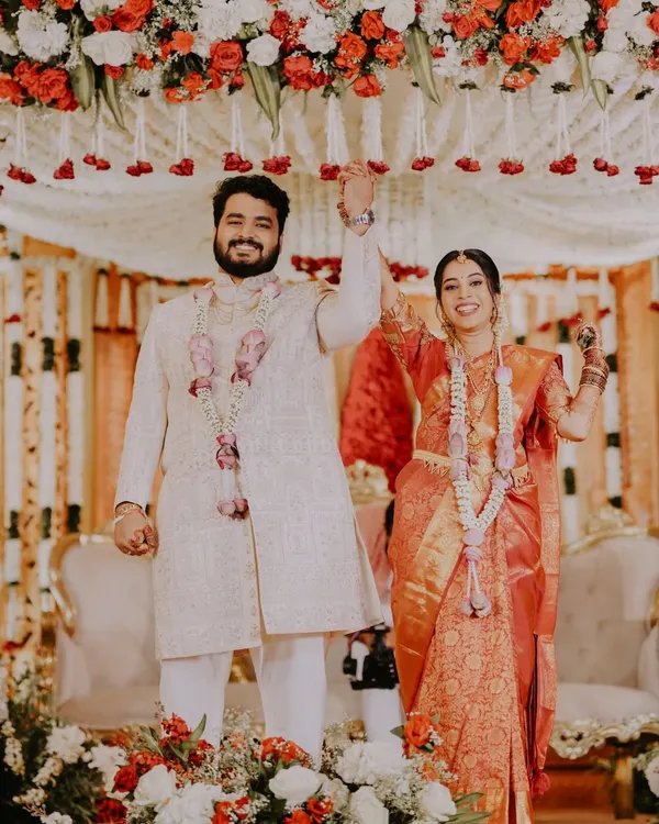 A moment of pure celebration as Yash and Jestha raise their hands in triumph after their South Indian wedding ceremony. The vibrant colors of the decor and their attire create a joyous and energetic scene.