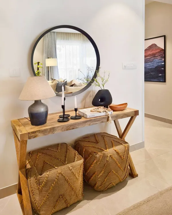 This entryway vignette in the Breeze Home proves you don't need a large foyer to make a great first impression. A slim console table, a round mirror, and pouffes that can double as extra seating create a nook that is both stylish and functional.
