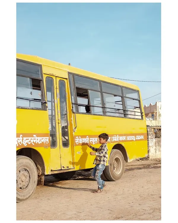 A young boy reaches for the side of a yellow school bus on a dusty road in Rajasthan. This is a simple, candid moment from my travels through the state.