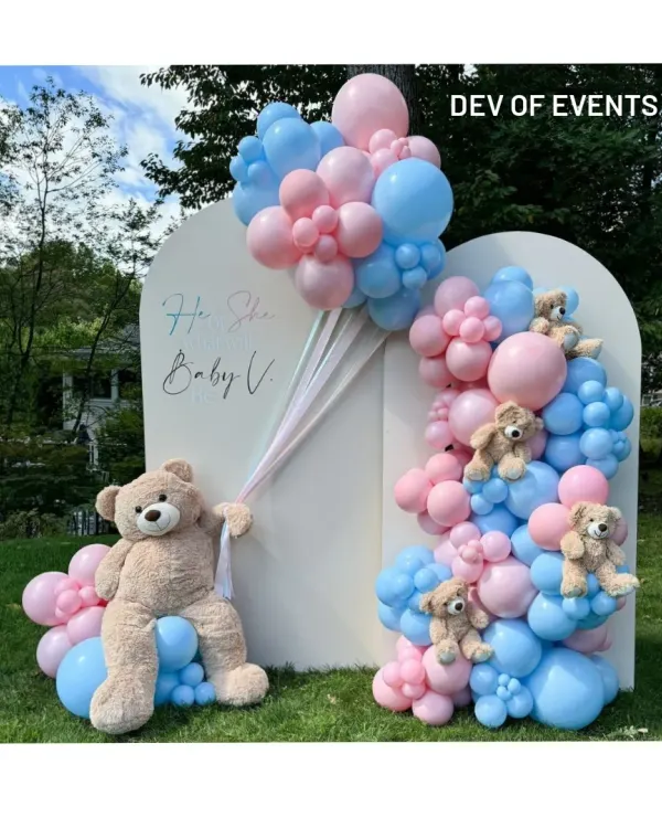 A classic "He or She" gender reveal baby shower. This outdoor setup features a clean white backdrop with pink and blue balloon garlands and adorable teddy bears.