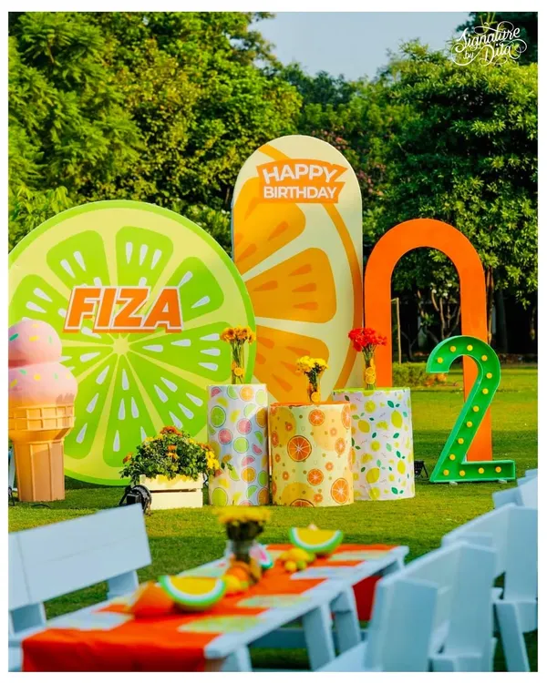 The main photo zone for a 'Two-tti Fruity' party, celebrating a second birthday. I designed oversized citrus slice backdrops, a personalized name sign, and a large light-up number '2' for a zesty and vibrant look.