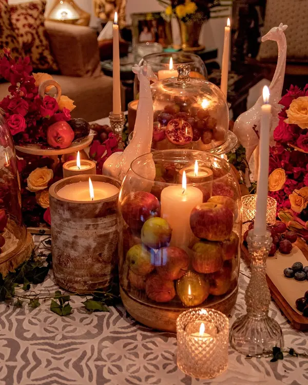 An opulent tablescape designed for an intimate wine and cheese evening. The scene is a rich tapestry of deep red florals, fresh fruits like apples and pomegranates, and an abundance of glowing candles, creating a warm and indulgent atmosphere.