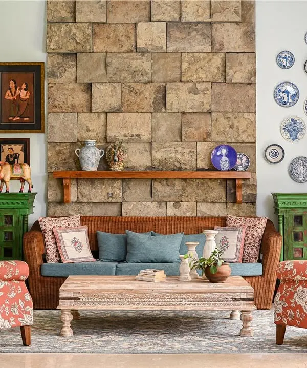 This living room is the heart of a rustic, medieval-inspired home. We brought in large, heavy stones to create a fireplace-like feature wall, balancing its weight with warm floral prints, hand-painted green cabinets, and a collection of the family's treasured Kalighat art.