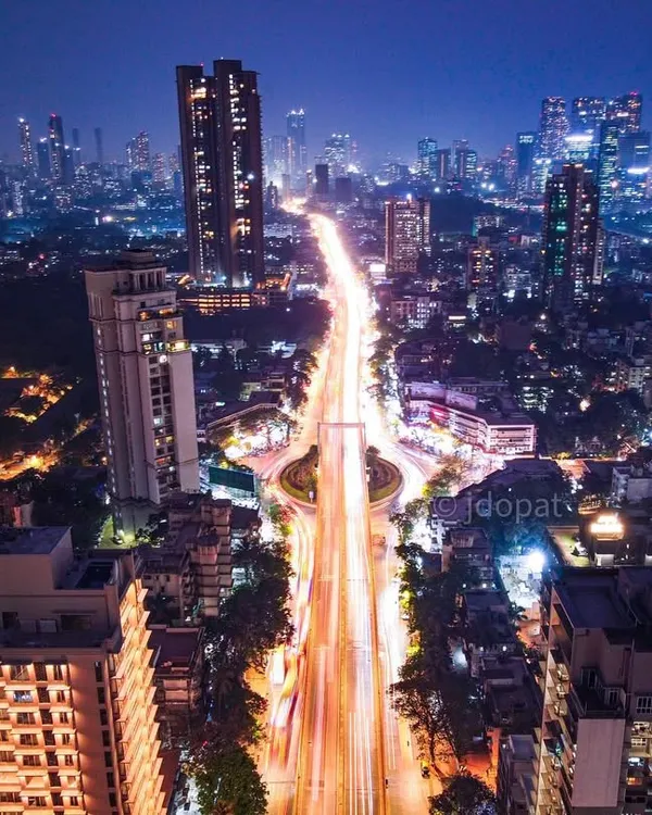 A high-angle, long-exposure drone shot of a major traffic circle in Mumbai at night, with light trails creating a sense of organized chaos.