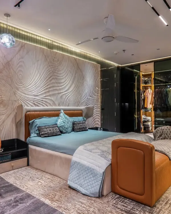 This bedroom features a stunning 3D carved accent wall that creates a sense of movement and artistry. The design is complemented by warm, ambient lighting, a custom leather bench, and rich, dark flooring for a truly unique and luxurious feel.