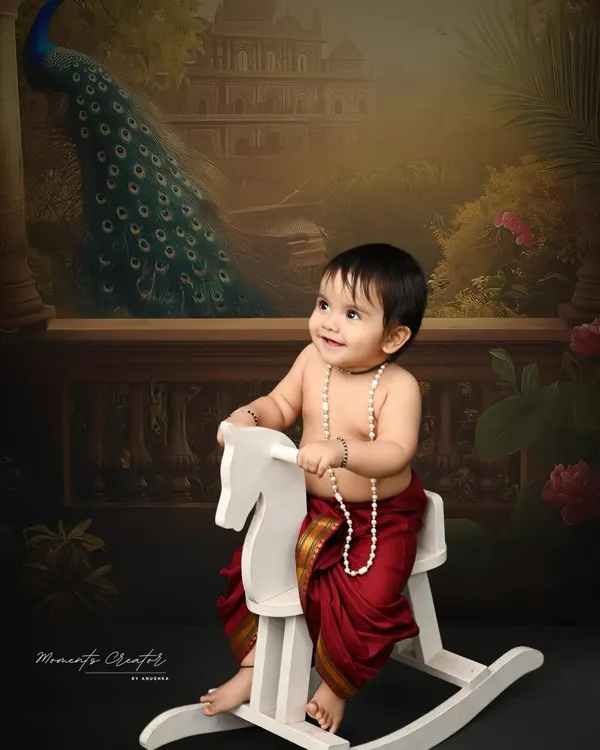 A little prince on his rocking horse. Dressed in a traditional dhoti, this baby boy looks regal and charming against a classic, painterly backdrop with a peacock.