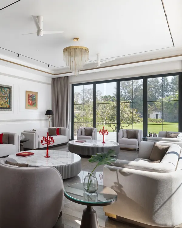 This formal living room is designed for large family gatherings, with ample seating and floor-to-ceiling windows that offer panoramic views of the garden. The neutral palette is punctuated by pops of red, creating a space that is both sophisticated and welcoming.