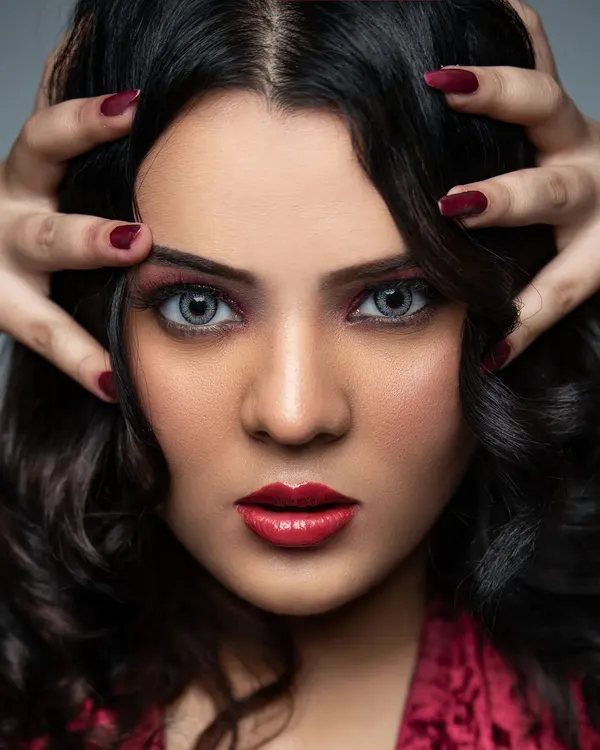 A striking beauty portrait focusing on a flawless, matte complexion and dramatic makeup. This look features bold red lips, subtle contouring, and intense eye makeup with a hint of red, complemented by grey contact lenses for a high-fashion editorial finish.